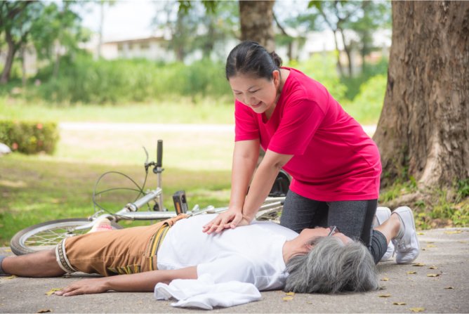 woman lying on grass under a tree, receiving CPR
